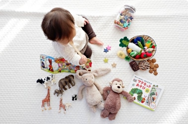 Baby sitting on a white blanket surrounded with toys