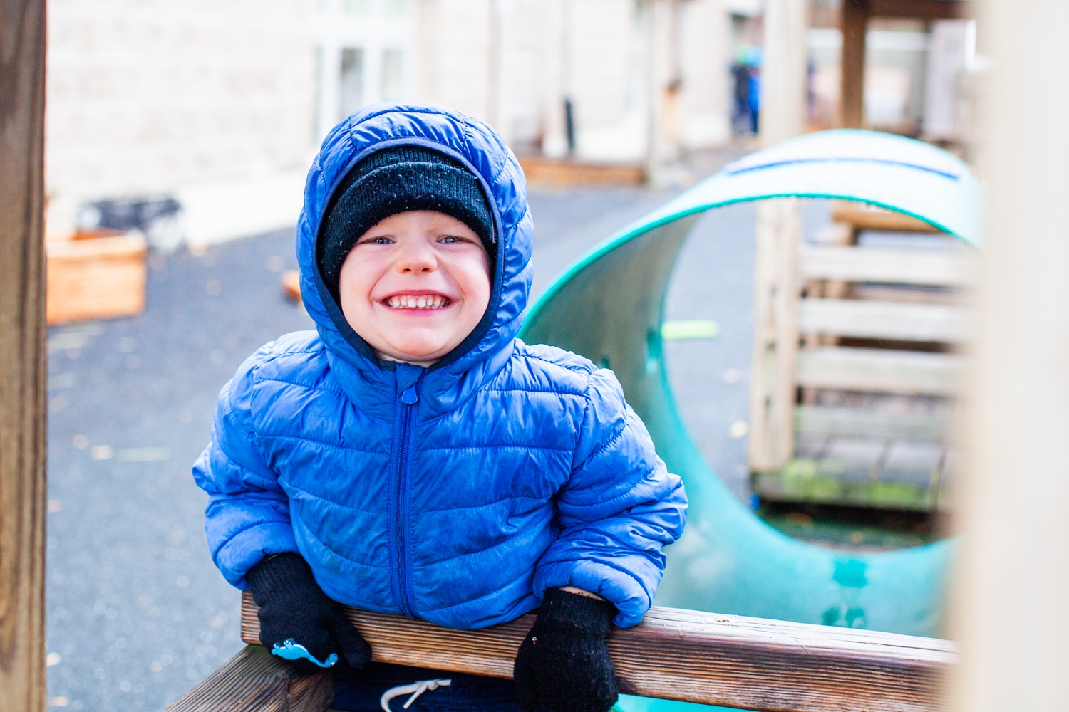 Child wearing blue coat and hoodie smiling at the camera while playing outside