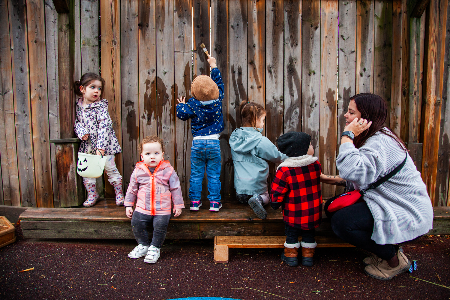 Infants sitting and standing on a bench outside with teacher
