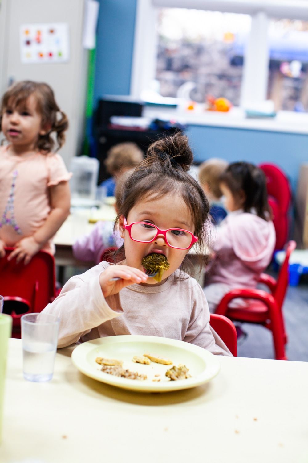 Girl with pink glasses eating broccoli