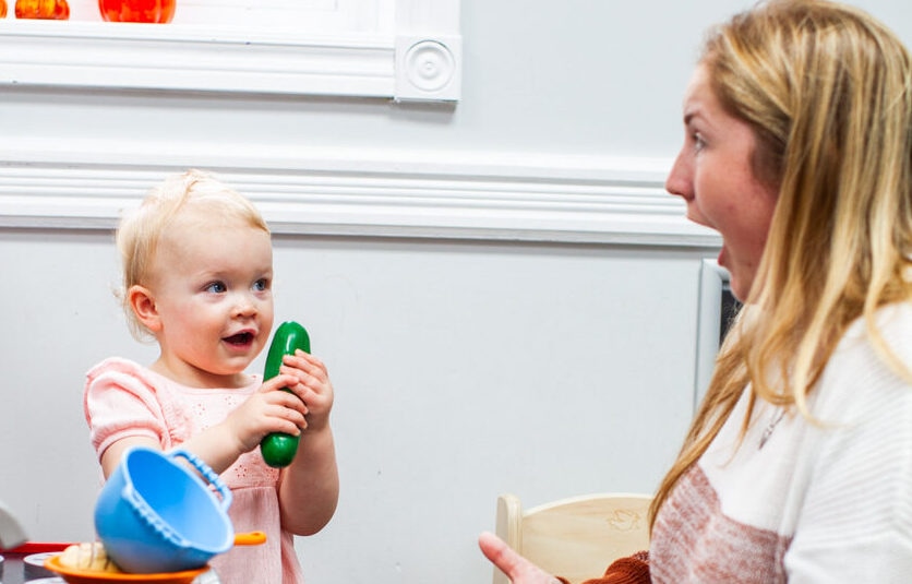 Happy infant shows toy cucumber to surprised adult