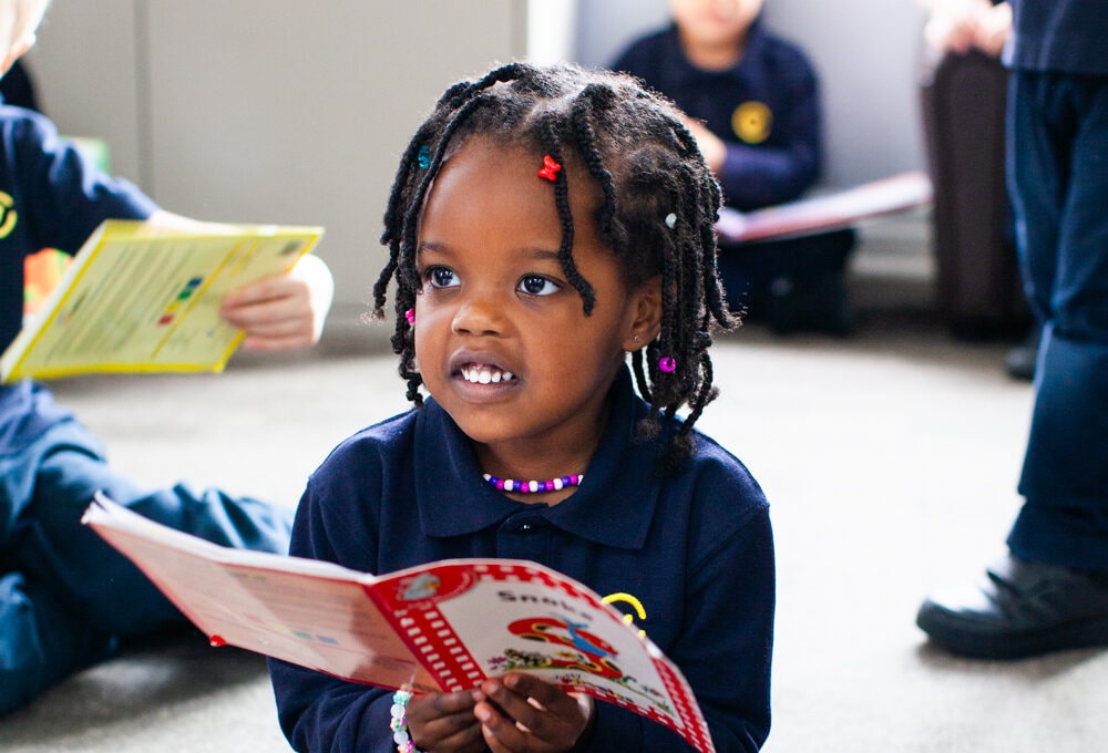 Girl holding a book while looking up at camera and smiling