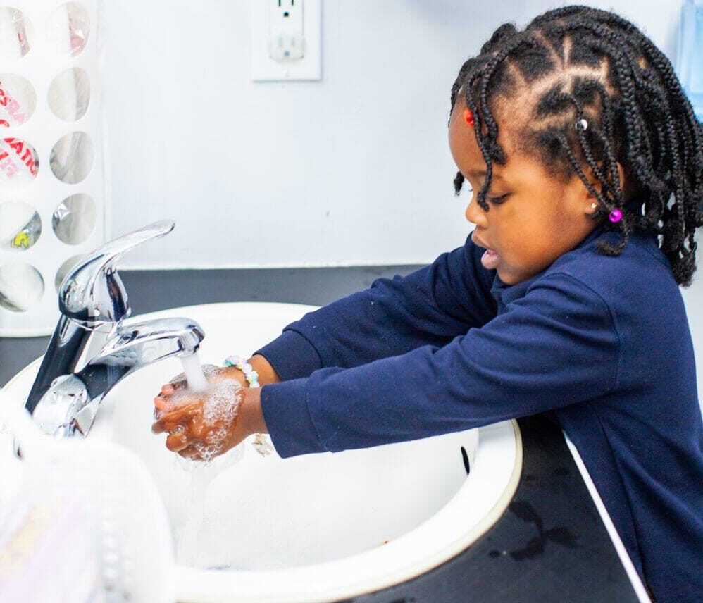 little girl standing at sink washing hands