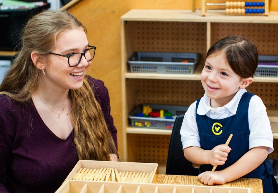 Adult sitting with child as child engages in Montessori activities