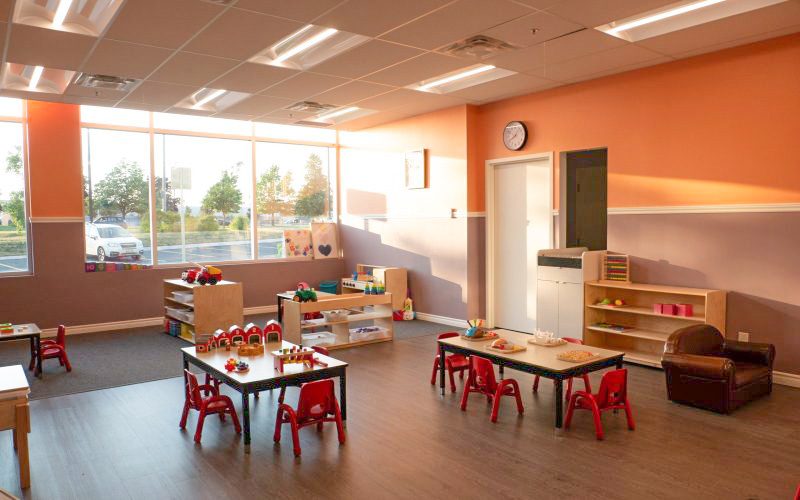 Classroom with tables, red chairs, big windows and shelves