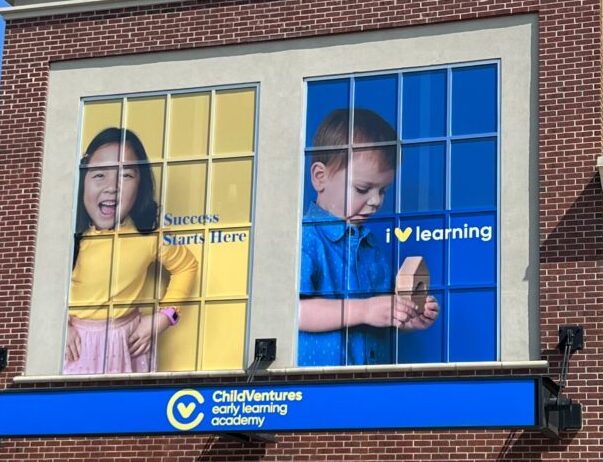 Building with a blue sign and two big windows with blue and yellow posters of children