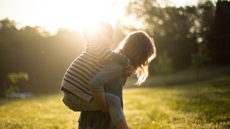 Girl carrying little boy on her back in a park